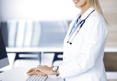 Bilinmeyen kadın doktor klinikteki resepsiyondaki masaüstü bilgisayarında daktilo çekiyor. Doktor iş yerinde, yakın plan. Tıp konsepti