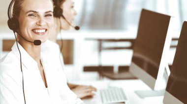 Sarışın kadın müşteri hizmetleri temsilcisi ve meslektaşı internetteki müşterilerine kulaklık kullanarak danışıyorlar. Çağrı merkezi ve iş adamları kavramı