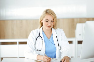 Hastanedeki ya da klinikteki masa başında oturan kadın doktor. Sarışın, neşeli doktor ilaç geçmişi formunu dolduruyor.