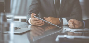 Bilinmeyen işadamı, modern ofisteki cam masada otururken tablet bilgisayar kullanıyor ve iş arkadaşıyla birlikte çalışıyor. Takım çalışması ve ortaklık kavramı