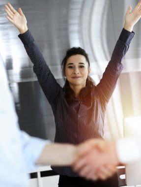 Toplantıdaki başarı anlaşması sayesinde mutlu ve heyecanlı iş kadını ellerini kaldırıyor. Sinsi ofiste el sıkışan iki adam.