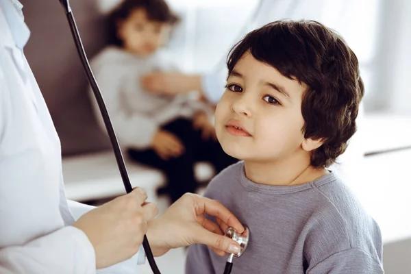 Dokter-vrouw die een kindpatiënt onderzoekt met stethoscoop. Leuke Arabische jongen en zijn broer op afspraak bij de dokter. Geneesmiddelenconcept — Stockfoto