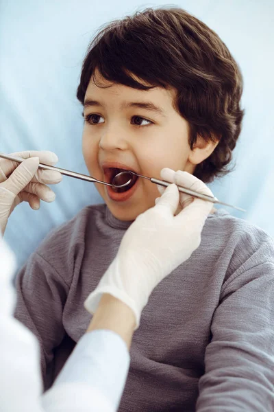 Pequeño chico árabe sentado en la silla dental con la boca abierta durante la revisión oral con el médico dentista. Concepto de estomatología — Foto de Stock