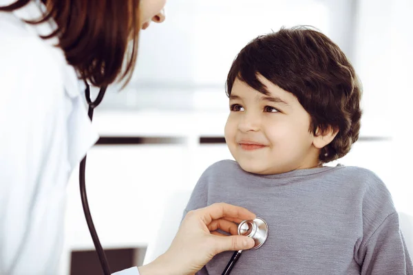 Médico-mujer examinando a un niño paciente por estetoscopio. Lindo chico árabe en la cita con el médico. Concepto de medicina —  Fotos de Stock