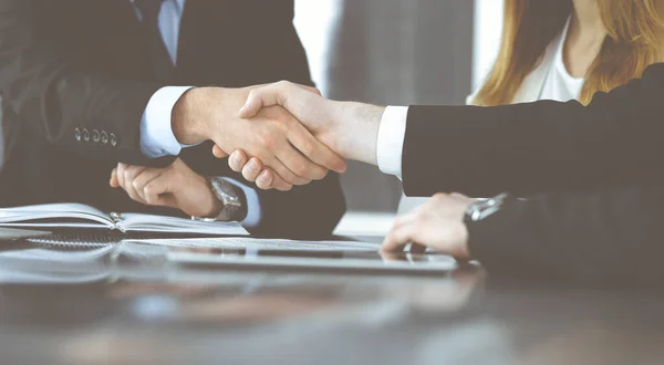 Unknown businessmen shaking hands above the glass desk in a modern office, close-up. Unknown business people at meeting. Teamwork, partnership and handshake concept