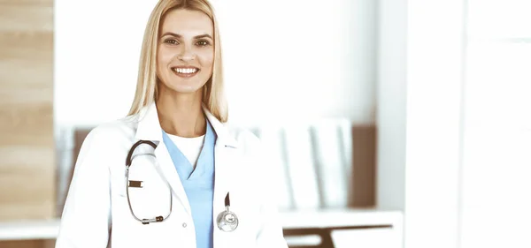 Médico-mujer en el trabajo en la clínica feliz de su profesión. La doctora rubia controla el historial de medicamentos y los resultados del examen médico. Concepto de medicina — Foto de Stock