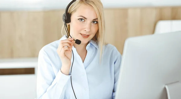 Mujer rubia de negocios sentada y comunicada por auriculares en la oficina del centro de llamadas. Concepto de negocio de telesales u ocupación de oficina en el hogar — Foto de Stock