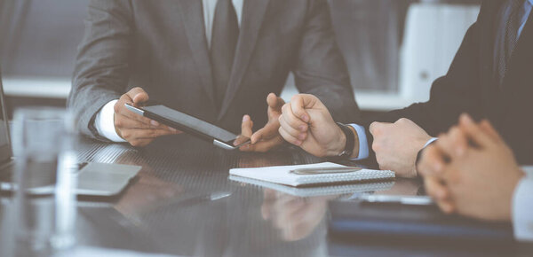 Unknown businessman using tablet computer and working together with his colleague while sits at the glass desk in modern office. Teamwork and partnership concept