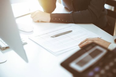 Mali durumu kontrol eden ya da vergi formları için hesap makinesinin geliri ile sayan, elleri yakın çekim. İş kadını ofisteki masada iş arkadaşıyla oturuyor ve çalışıyor. Vergi ve Denetim kavramı