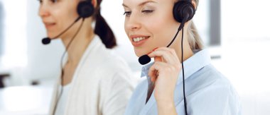Sarışın kadın çağrı operatörü müşterilere danışmak için bilgisayar ve kulaklık kullanıyor. Müşteri hizmetleri işgali olarak çalışan bir grup insan. İş konsepti