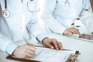 İş yerindeki bilinmeyen kadın doktorlar, arka planda hastaları var. Hastane resepsiyonunda beklerken tıbbi belgeleri dolduran kadın doktorlar, yakın plan. Sağlık hizmeti kavramı