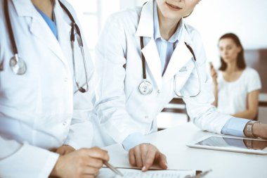 İşteki iki kadın doktor ve hasta arka planda. Hastane resepsiyonunda beklerken tıbbi belgeleri dolduran kadın doktorlar. Tıptaki veriler