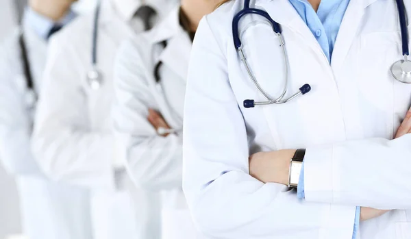 Modern orvosok csoportja áll, mint egy csapat keresztbe tett karokkal a kórházi irodában. Orvosi segítség, biztosítás az egészségügyben, a legjobb betegségkezelés és az orvostudomány koncepciója — Stock Fotó