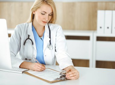 Hastanedeki ya da klinikteki masa başında oturan kadın doktor. Sarışın, neşeli doktor ilaç geçmişi formunu dolduruyor.