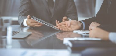 Bilinmeyen işadamı, modern ofisteki cam masada otururken tablet bilgisayar kullanıyor ve iş arkadaşıyla birlikte çalışıyor. Takım çalışması ve ortaklık kavramı