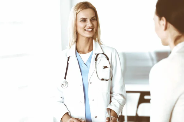 A kórházban dolgozó nő-orvos boldogan kommunikál a női beteggel. A szőke orvos ellenőrzi a kórtörténetét és a vizsgaeredményeit. Orvosi fogalom — Stock Fotó