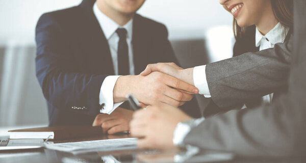 Неизвестный бизнесмен пожимает руку коллеге или партнеру над стеклянным столом в современном офисе крупным планом. Группа деловых людей на встрече