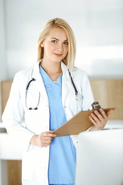 Женщина-врач, стоящая в больнице или клинике и заполняющая историю болезни. Данные и лучший сервис в медицине и здравоохранении — стоковое фото