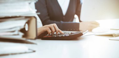 Mali durumu kontrol eden ya da vergi formları için hesap makinesinin geliri ile sayan, elleri yakın çekim. İş kadını ofisteki masada iş arkadaşıyla oturuyor ve çalışıyor. Vergi ve Denetim kavramı