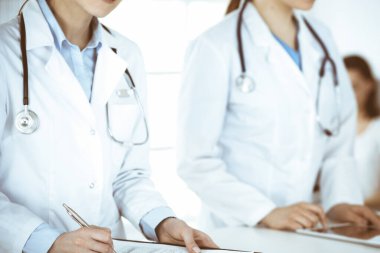 İş yerindeki bilinmeyen kadın doktorlar, arka planda hastaları var. Hastane resepsiyonunda beklerken tıbbi belgeleri dolduran kadın doktorlar, yakın plan. Sağlık hizmeti kavramı