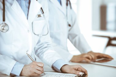 İş yerindeki bilinmeyen kadın doktorlar, arka planda hastaları var. Hastane resepsiyonunda beklerken tıbbi belgeleri dolduran kadın doktorlar, yakın plan. Sağlık hizmeti kavramı