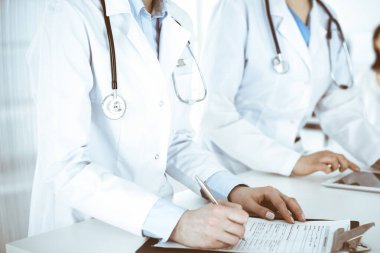 İş yerindeki bilinmeyen kadın doktorlar, arka planda hastaları var. Hastane resepsiyonunda beklerken tıbbi belgeleri dolduran kadın doktorlar, yakın plan. Sağlık hizmeti kavramı