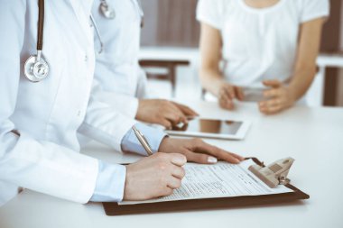 İş yerindeki bilinmeyen kadın doktorlar hastalara danışıyor. Tıbbi belge ya da reçete dolduran kadın doktorlar, yakın çekim. Sağlık hizmeti kavramı