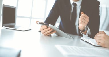Bilinmeyen iş adamları modern ofiste tablet bilgisayar kullanıyorlar. İş adamı ya da erkek girişimci, çalışma masasında meslektaşıyla birlikte çalışıyor.