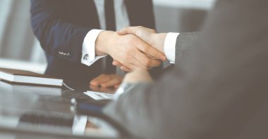 Bilinmeyen işadamı, modern ofiste iş arkadaşı ya da ortağıyla el sıkışıyor. Toplantıda iş adamları grubu