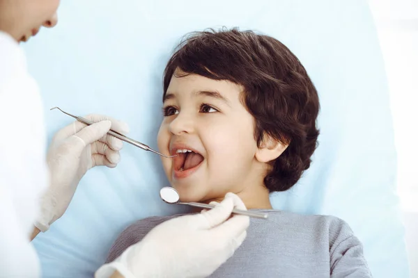 Lindo chico árabe sentado en la silla dental con la boca abierta durante el control oral con el médico. Visita al consultorio del dentista. Concepto de estomatología — Foto de Stock