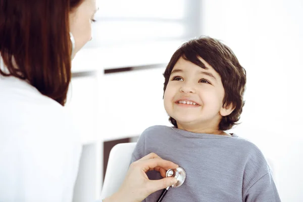 Médico-mujer examinando a un niño paciente por estetoscopio. Lindo chico árabe en la cita con el médico. Concepto de medicina —  Fotos de Stock