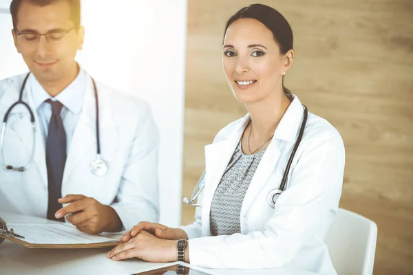 Two doctors discussing treatment problems while sitting at the desk in sunny office