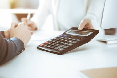 Mali durumu kontrol eden ya da vergi formları için hesap makinesinin geliri ile sayan, elleri yakın çekim. İş kadını ofisteki masada iş arkadaşıyla oturuyor ve çalışıyor. Vergi ve Denetim kavramı