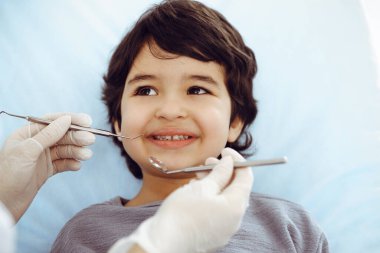 Tatlı Arap çocuk doktorla sözlü kontrol sırasında ağzı açık bir şekilde dişçi koltuğunda oturuyor. Dişçi muayenehanesi. Stomatoloji kavramı