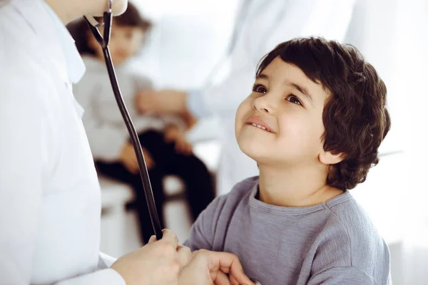 Ärztin untersucht eine Kinderpatientin mit einem Stethoskop. Netter arabischer Junge und sein Bruder beim Arzttermin. Medizinkonzept — Stockfoto