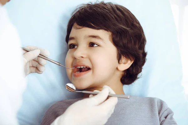 Cute arab boy sitting at dental chair with open mouth during oral checking up with doctor. Visiting dentist office. Stomatology concept — Stock Photo, Image