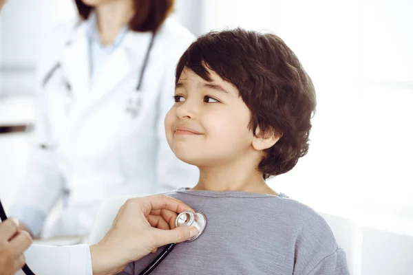 Doctor-woman examining a child patient by stethoscope. Cute arab boy at physician appointment. Medicine concept — Stock Photo, Image