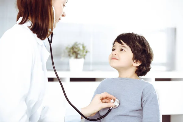Médico-mujer examinando a un niño paciente por estetoscopio. Lindo chico árabe en la cita con el médico. Concepto de medicina —  Fotos de Stock