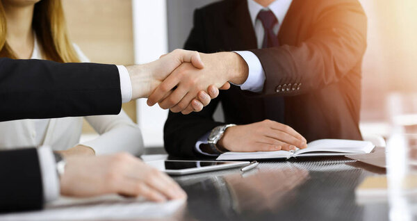 Businessman shaking hands with his colleague above the glass desk in sunny modern office, close-up. Unknown business people at meeting