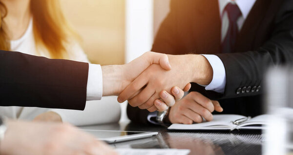Businessman shaking hands with his colleague above the glass desk in sunny modern office, close-up. Unknown business people at meeting