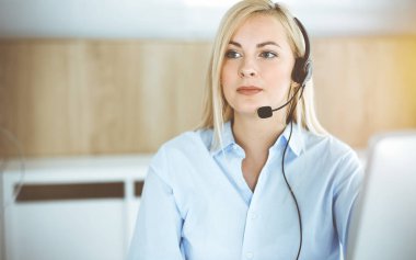 Sarışın iş kadını güneşli ofisteki çağrı merkezinde oturup kulaklıkla iletişim kuruyor. Teleskop işi kavramı