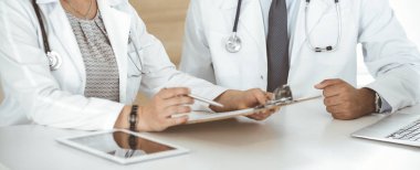 İki bilinmeyen doktor hastane ofisinde masa başında otururken tedavi sorunlarını tartışıyor, yakın plan. Tıptaki veriler