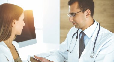 Doktor ve hasta güneşli klinikteki masada otururken tıbbi muayene sonuçlarını tartışıyorlar.