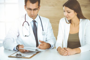 Doktor ve hasta güneşli klinikteki masada otururken tıbbi muayene sonuçlarını tartışıyorlar.