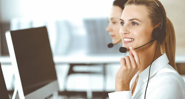 Blond female customer service representative and her colleague are consulting clients online using headset. Call center and business people concept