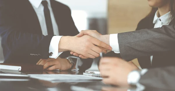 Hombre de negocios desconocido estrechando la mano con su colega o compañero por encima del escritorio de cristal en la oficina moderna, de cerca. Grupo de empresarios en la reunión — Foto de Stock