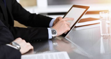 Businessman using tablet computer and work together with his colleague in sunny modern office, close-up. Unknown business people at meeting. Teamwork and partnership concept