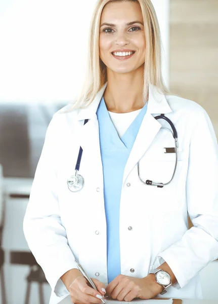 Kvinnoläkare på kliniken glad över sitt yrke. Blond kvinnlig läkare kontrollerar sjukdomshistoria och resultat medicinsk undersökning. Medicinskt koncept — Stockfoto