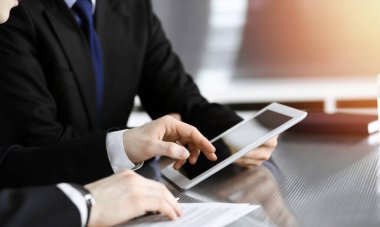 Businessman using tablet computer and work together with his colleague in sunny modern office, close-up. Unknown business people at meeting. Teamwork and partnership concept