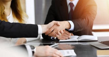 İş adamı, güneşli modern ofiste cam masanın üstünde meslektaşıyla tokalaşıyor. Yakın plan. Toplantıda bilinmeyen iş adamları